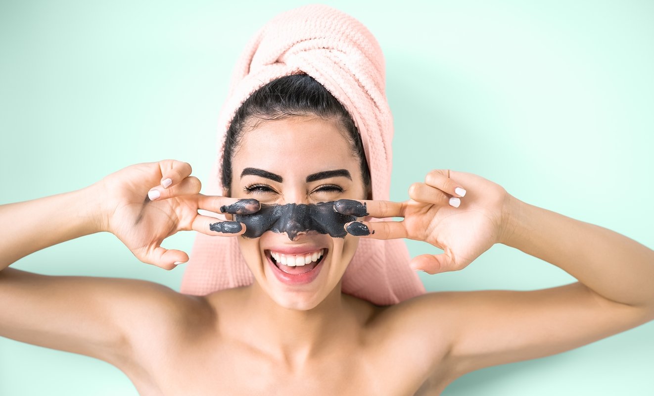 Imagem de mulher com toalha na cabeça e com mascara de argila preta no rosto.